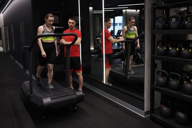 Photo of Young woman exercising on treadmill with professional personal trainer in gym