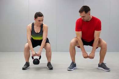 Photo of Young woman exercising with kettlebell with professional personal trainer in gym