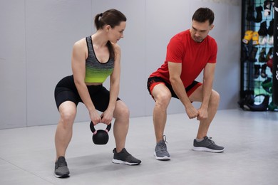 Photo of Young woman exercising with kettlebell with professional personal trainer in gym