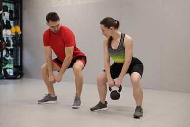 Photo of Young woman exercising with kettlebell with professional personal trainer in gym
