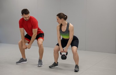 Photo of Young woman exercising with kettlebell with professional personal trainer in gym