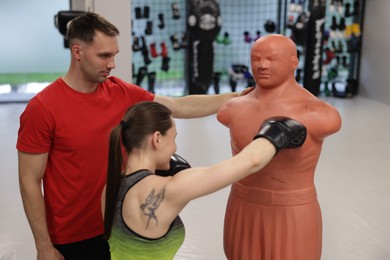 Photo of Young woman exercising with punching dummy with professional personal trainer in gym