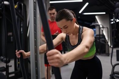 Photo of Young woman exercising with cable machine with professional personal trainer in gym