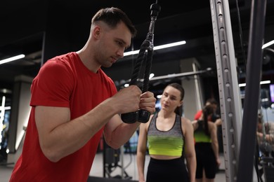 Photo of Professional personal trainer showing young woman how to exercise with lat pulldown machine in gym