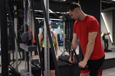 Photo of Professional personal trainer showing young woman how to exercise with lat pulldown machine in gym