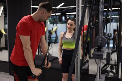 Photo of Professional personal trainer showing young woman how to exercise with lat pulldown machine in gym