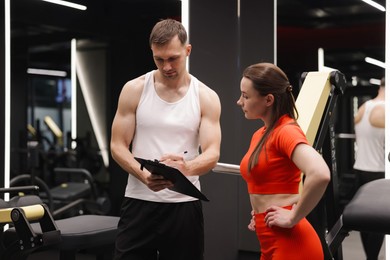 Photo of Young woman with professional personal trainer in gym
