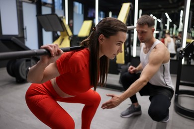 Photo of Young woman exercising with barbell with professional personal trainer in gym