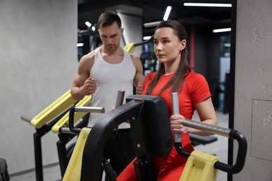 Photo of Young woman exercising on seated row machine with professional personal trainer in gym