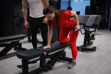 Photo of Young woman exercising with dumbbells with professional personal trainer in gym