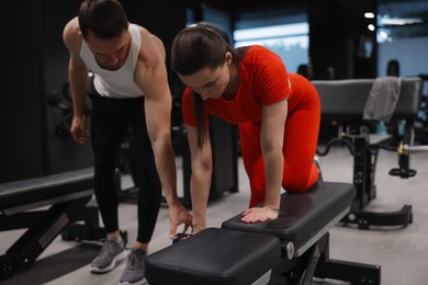 Photo of Young woman exercising with dumbbells with professional personal trainer in gym
