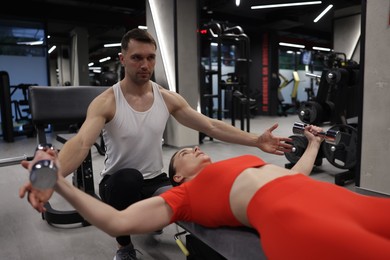 Photo of Young woman exercising with dumbbells with professional personal trainer in gym