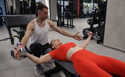 Photo of Young woman exercising with dumbbells with professional personal trainer in gym