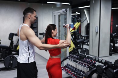 Photo of Young woman exercising with dumbbells with professional personal trainer in gym