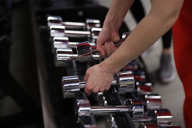 Photo of Woman taking dumbbells from stand in gym, closeup