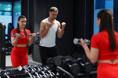 Photo of Young woman exercising with dumbbells with professional personal trainer in gym