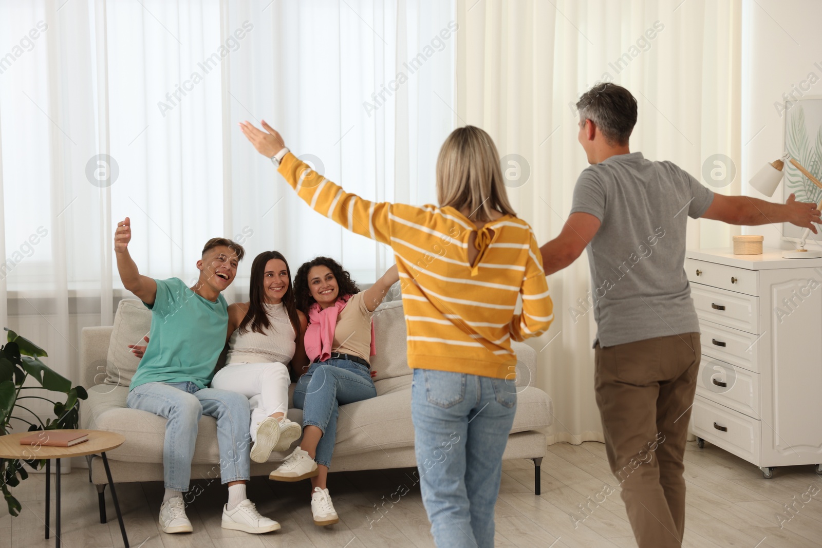 Happy friends greeting couple on sofa at home Photo of Happy friends greeting couple on sofa at home