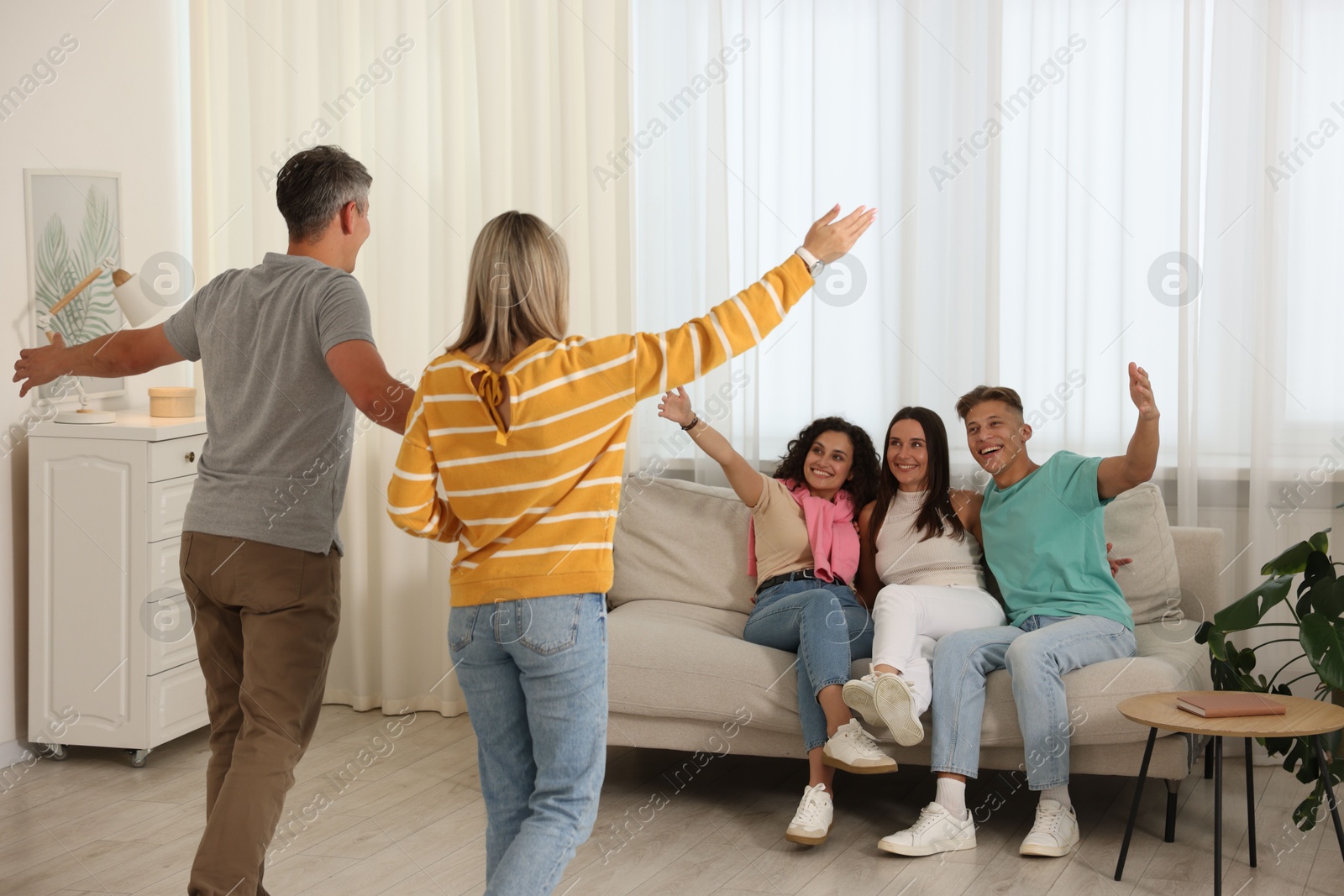 Happy friends greeting couple on sofa at home Photo of Happy friends greeting couple on sofa at home