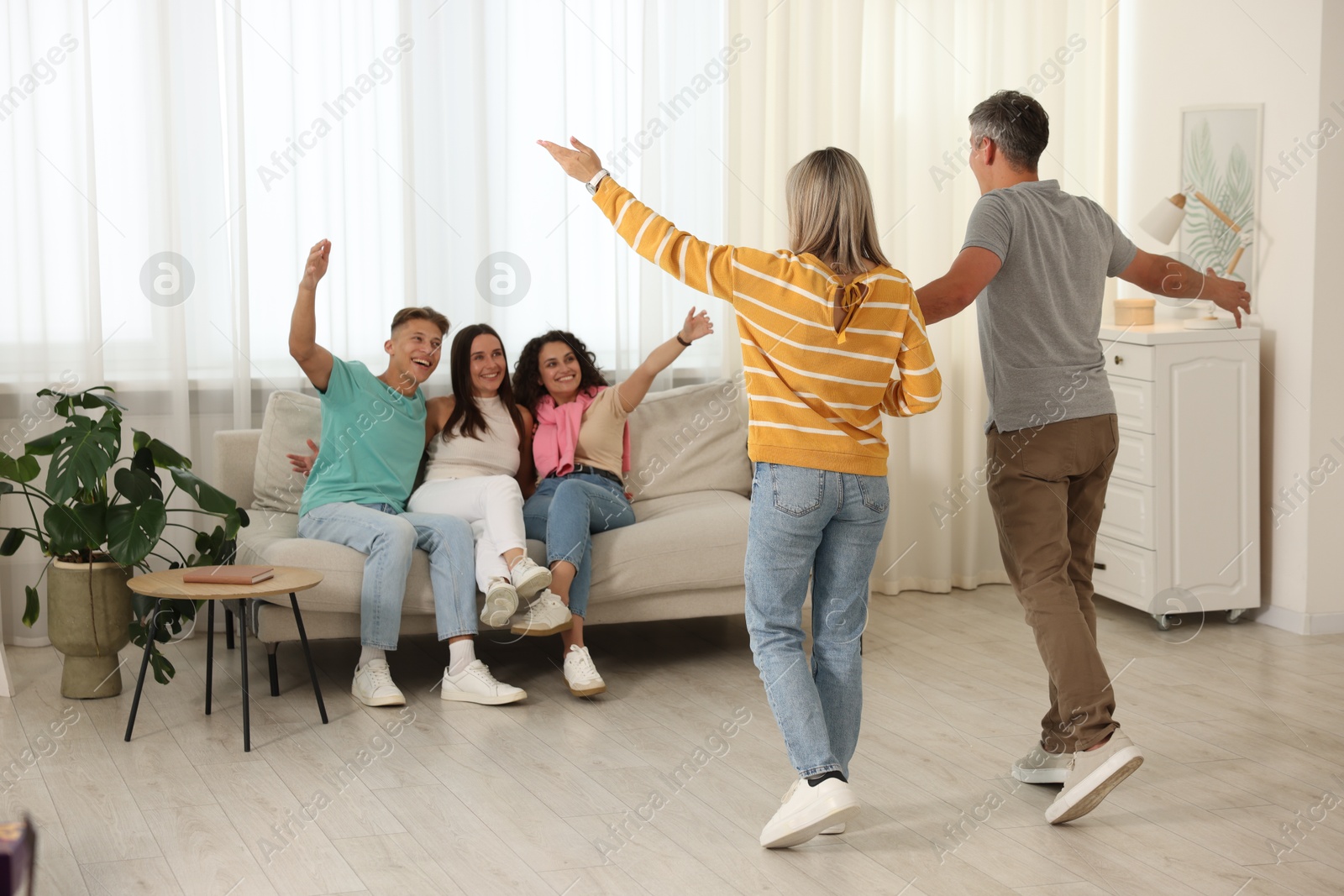 Happy friends greeting couple on sofa at home Photo of Happy friends greeting couple on sofa at home