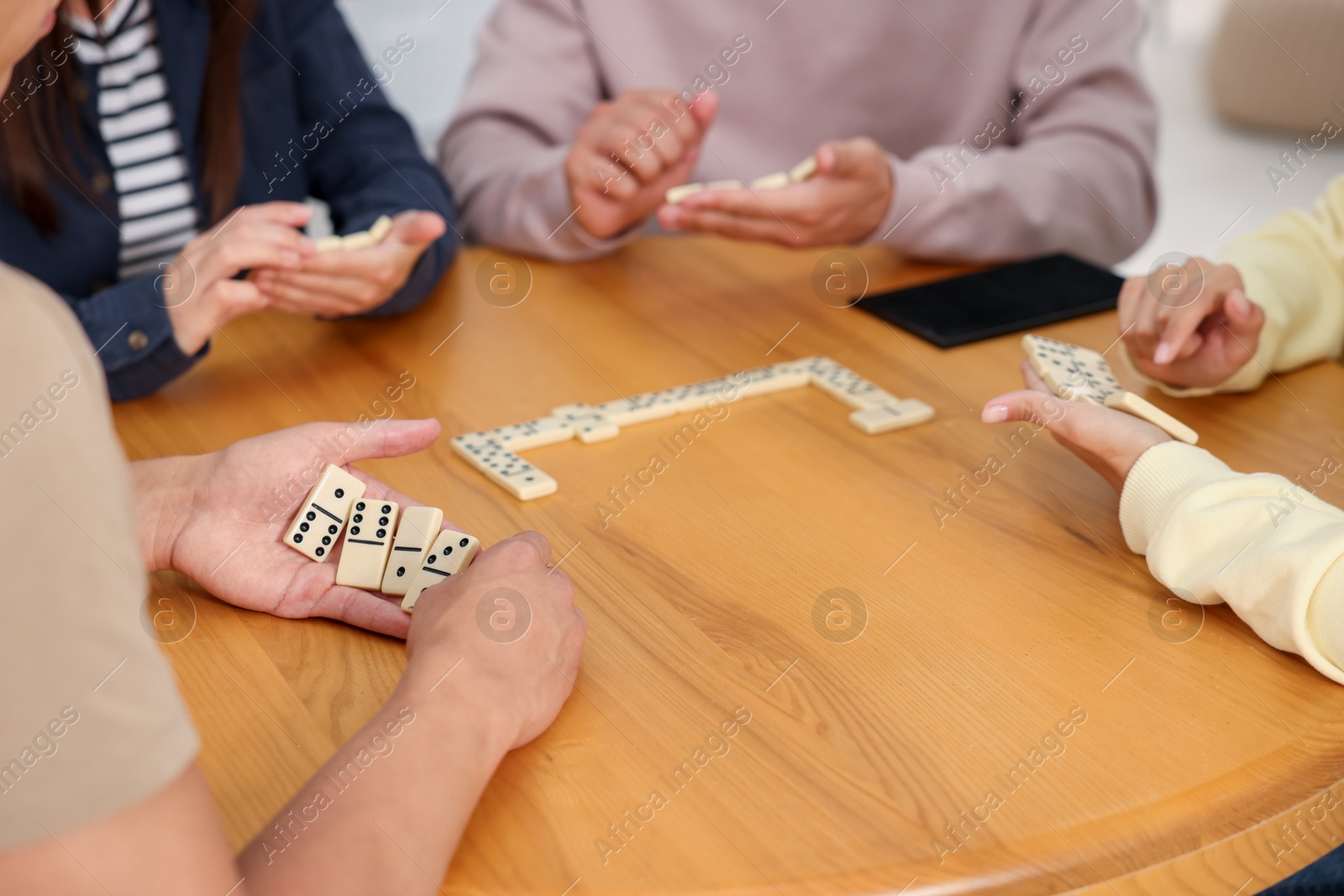 Friends playing dominoes at wooden table indoors, closeup Photo of Friends playing dominoes at wooden table indoors, closeup