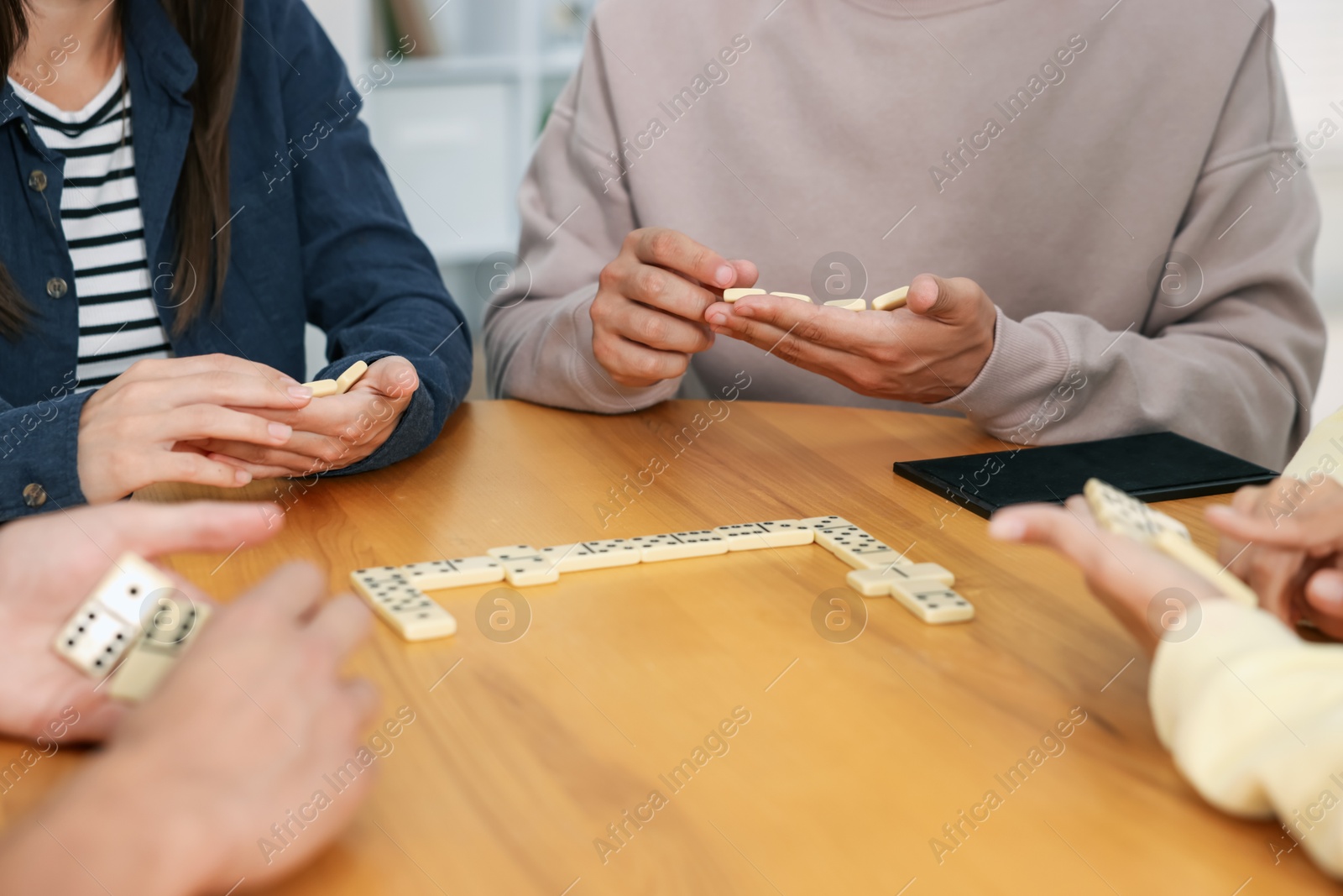 Friends playing dominoes at wooden table indoors, closeup Photo of Friends playing dominoes at wooden table indoors, closeup