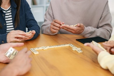 Photo of Friends playing dominoes at wooden table indoors, closeup