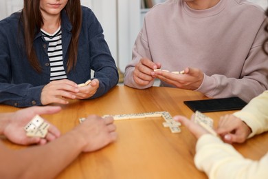 Photo of Friends playing dominoes at wooden table indoors, closeup