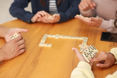 Photo of Friends playing dominoes at wooden table, closeup