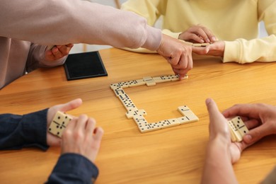 Photo of Friends playing dominoes at wooden table, closeup
