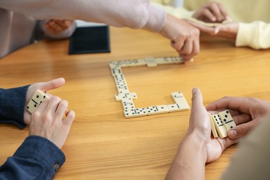 Photo of Friends playing dominoes at wooden table, closeup
