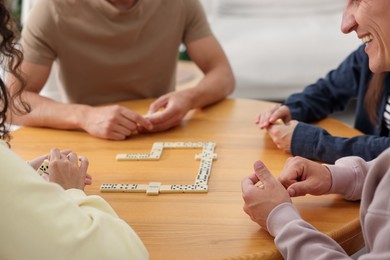 Photo of Friends playing dominoes at wooden table indoors, closeup