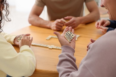 Photo of Friends playing dominoes at wooden table indoors, closeup