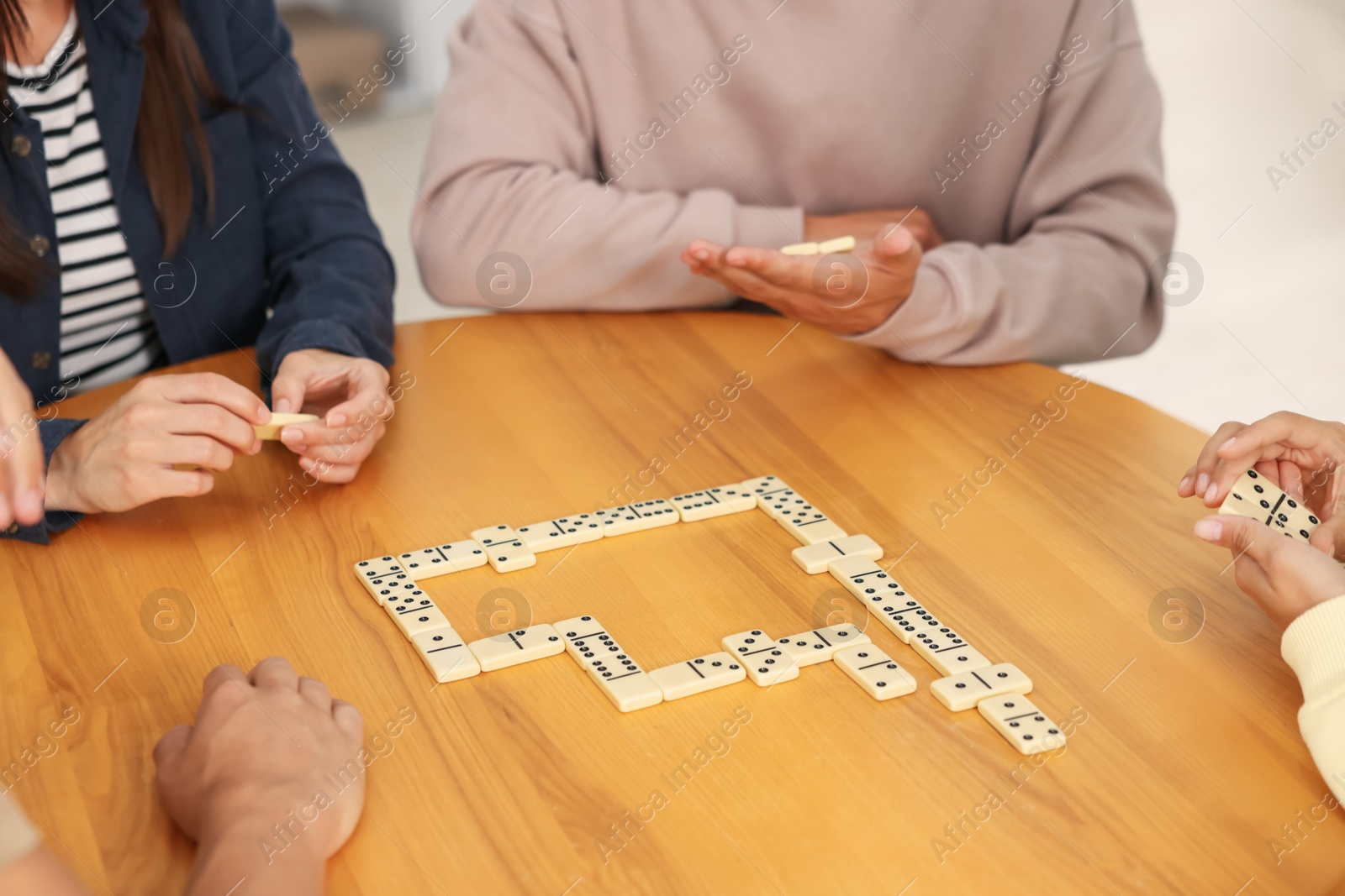 Friends playing dominoes at wooden table, closeup Photo of Friends playing dominoes at wooden table, closeup