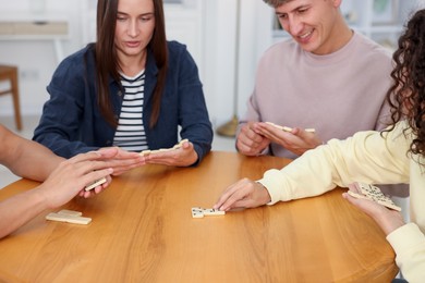 Photo of Friends playing dominoes at wooden table indoors, closeup