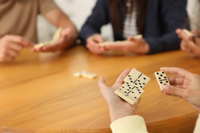 Photo of Friends playing dominoes at wooden table, closeup