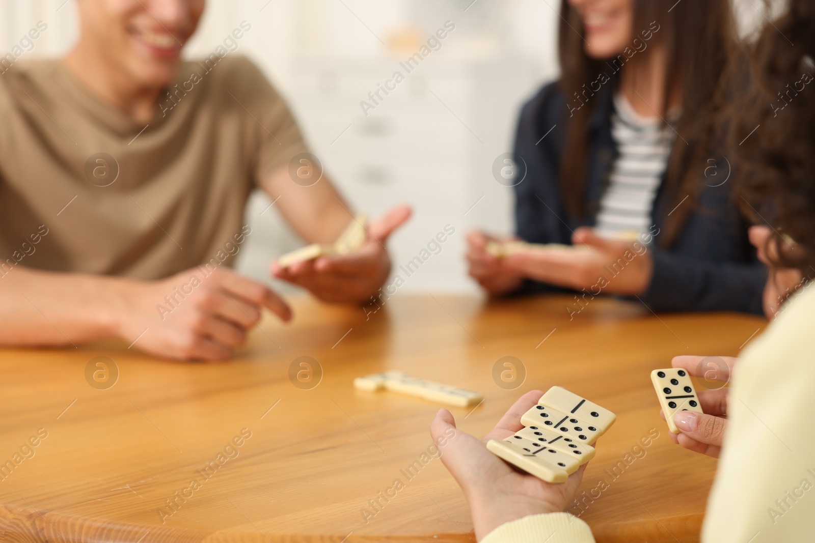 Friends playing dominoes at wooden table indoors, closeup Photo of Friends playing dominoes at wooden table indoors, closeup