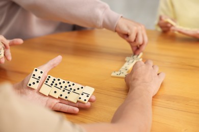Photo of Friends playing dominoes at wooden table, closeup