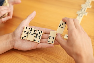 Photo of Friends playing dominoes at wooden table, closeup