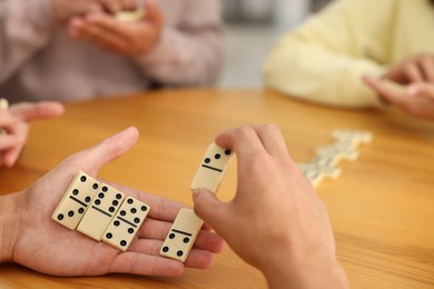 Photo of Friends playing dominoes at wooden table indoors, closeup
