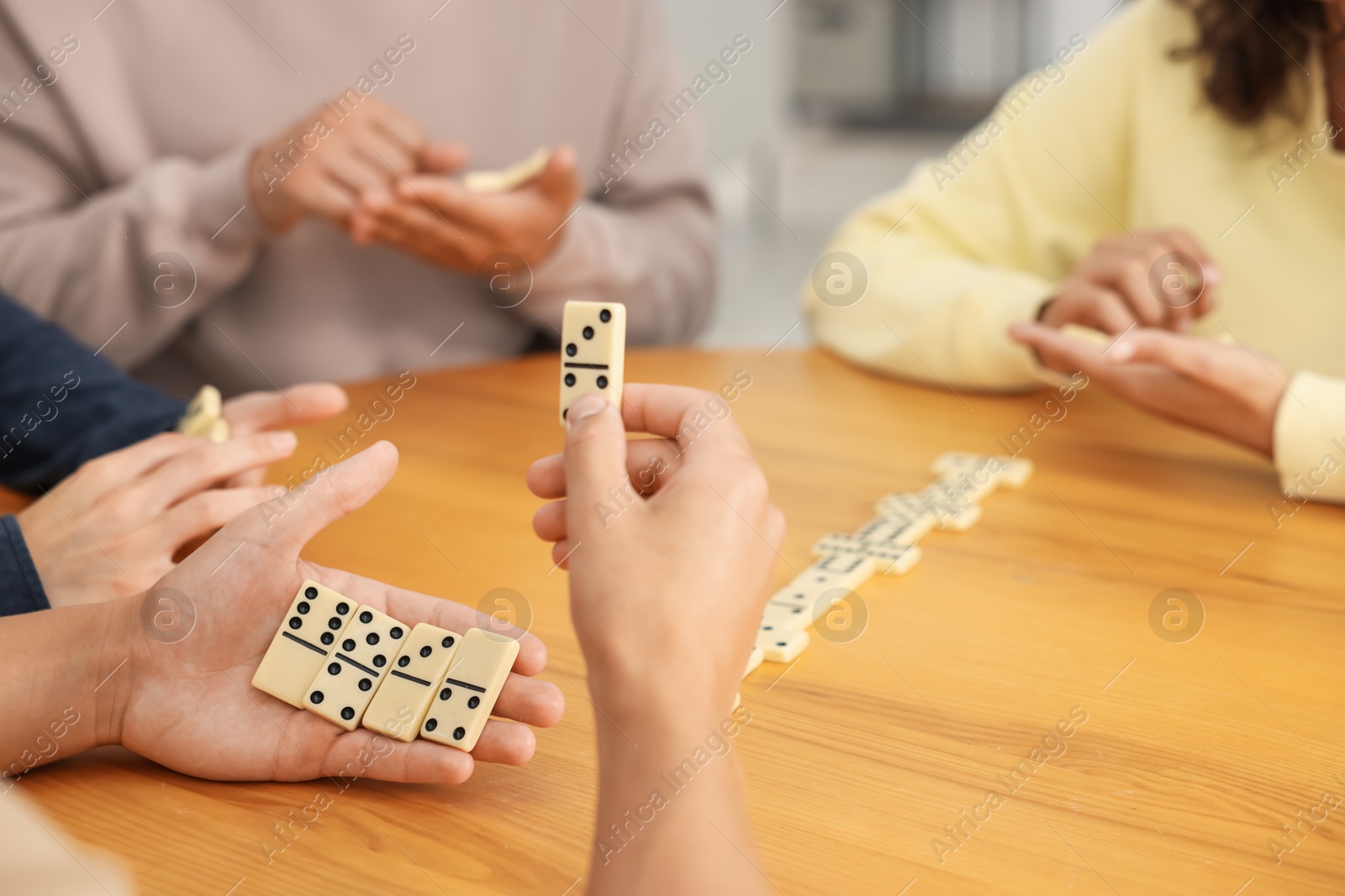 Friends playing dominoes at wooden table indoors, closeup Photo of Friends playing dominoes at wooden table indoors, closeup