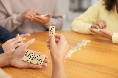 Photo of Friends playing dominoes at wooden table indoors, closeup