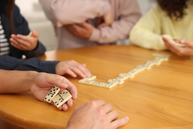 Photo of Friends playing dominoes at wooden table, closeup