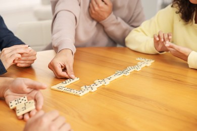 Photo of Friends playing dominoes at wooden table, closeup