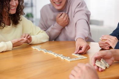 Photo of Happy friends playing dominoes at wooden table indoors, closeup