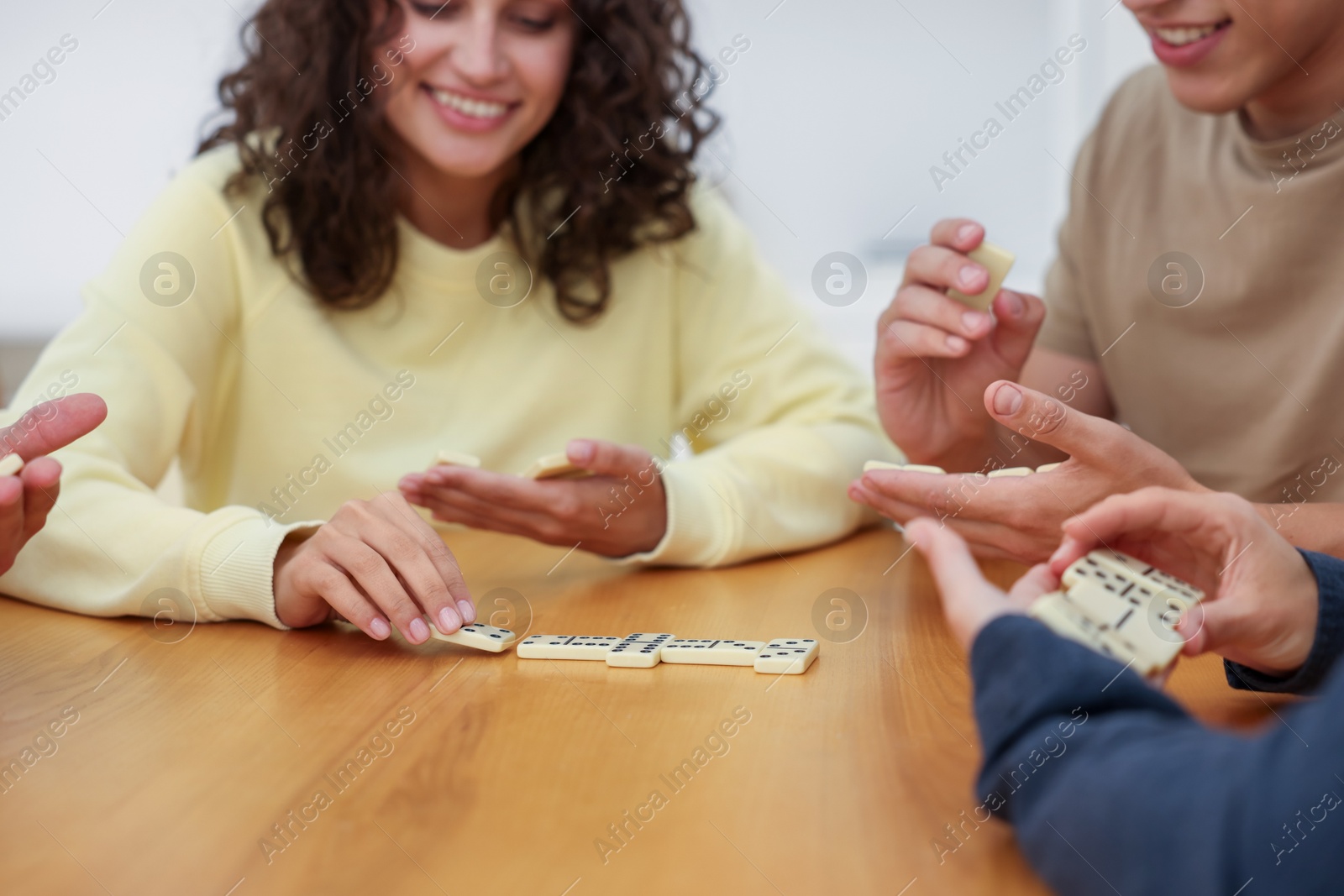 Happy friends playing dominoes at wooden table indoors, closeup Photo of Happy friends playing dominoes at wooden table indoors, closeup