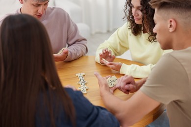 Photo of Friends playing dominoes at wooden table indoors