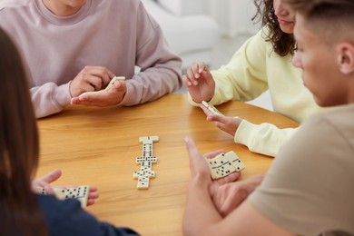 Photo of Friends playing dominoes at wooden table indoors, closeup