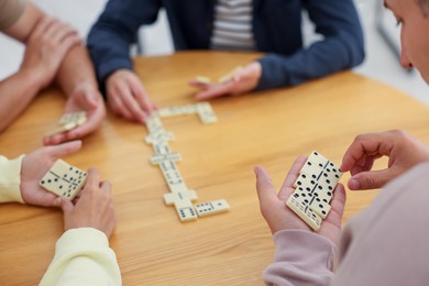 Photo of Friends playing dominoes at wooden table, closeup