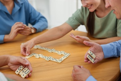 Photo of Happy friends playing dominoes at wooden table indoors, closeup
