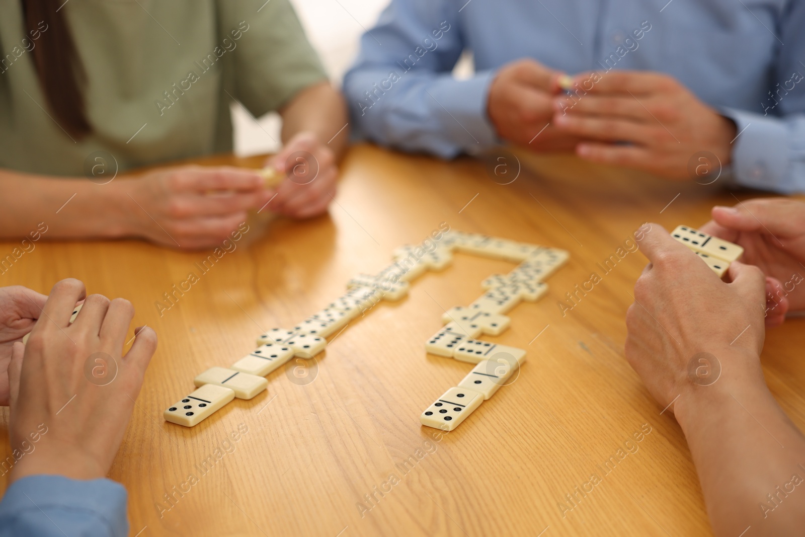 Friends playing dominoes at wooden table, closeup Photo of Friends playing dominoes at wooden table, closeup